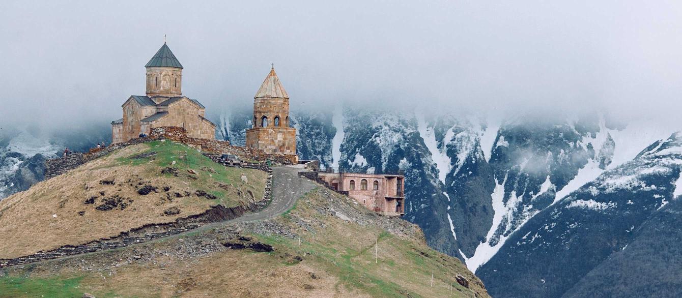 Medieval church on grassy hilltop surrounded by majestic mountains