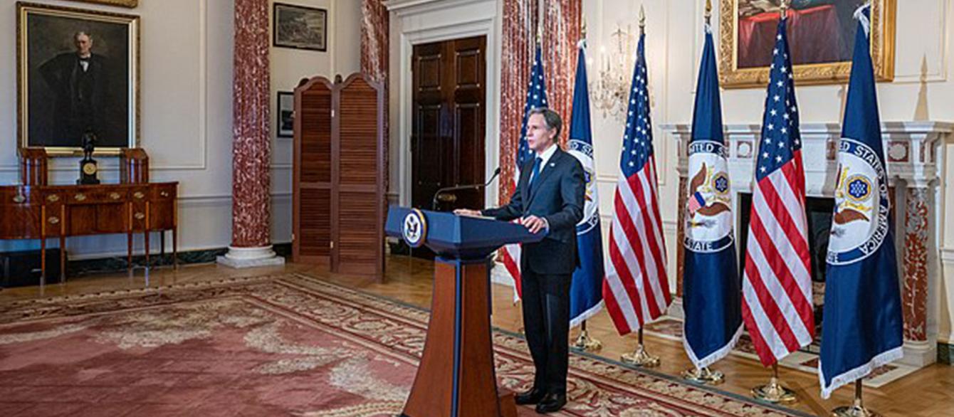 Secretary Blinken speaks at the podium in the background of American flags