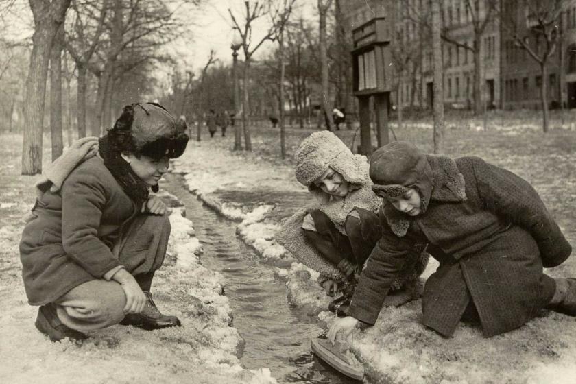 Boys launch toy boat in stream of melted snow