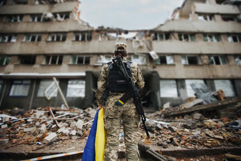 Ukrainian military woman with the Ukrainian flag in her hands on the background of an exploded house.
